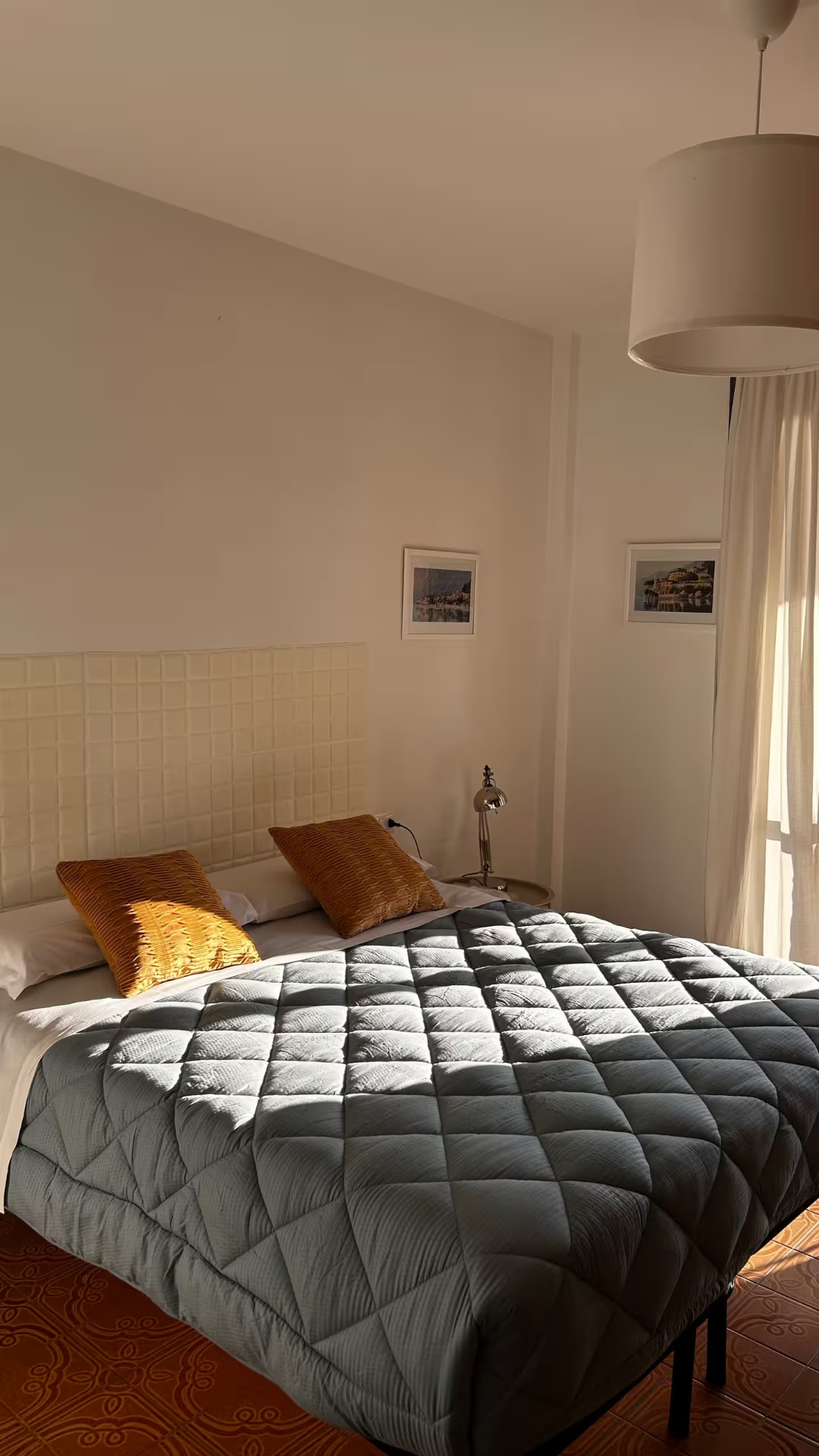 Double bed with a quilted headboard and mustard cushions in the afternoon sun