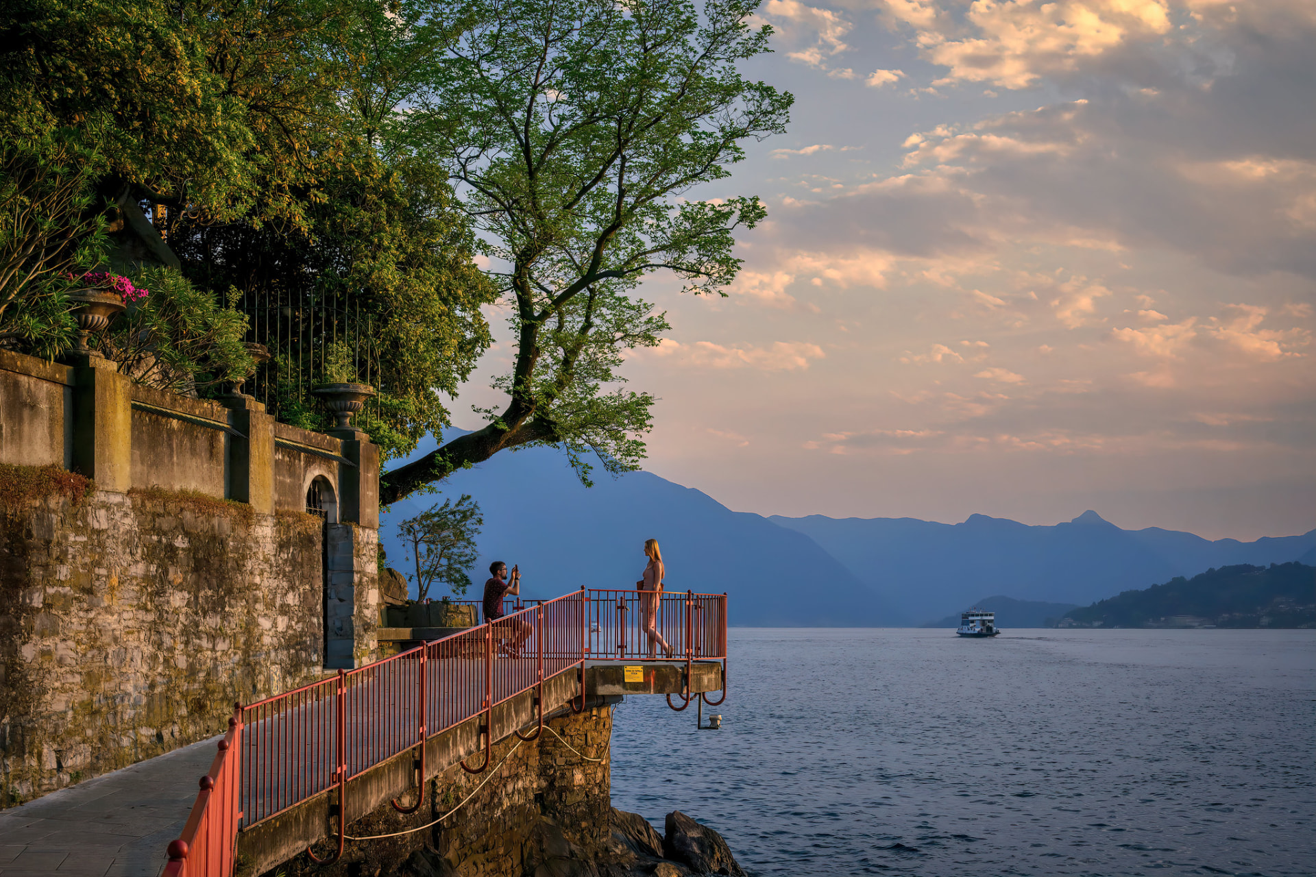 The lakeside promenade in Varenna at golden hour, with the open lake and mountain ridges beyond
