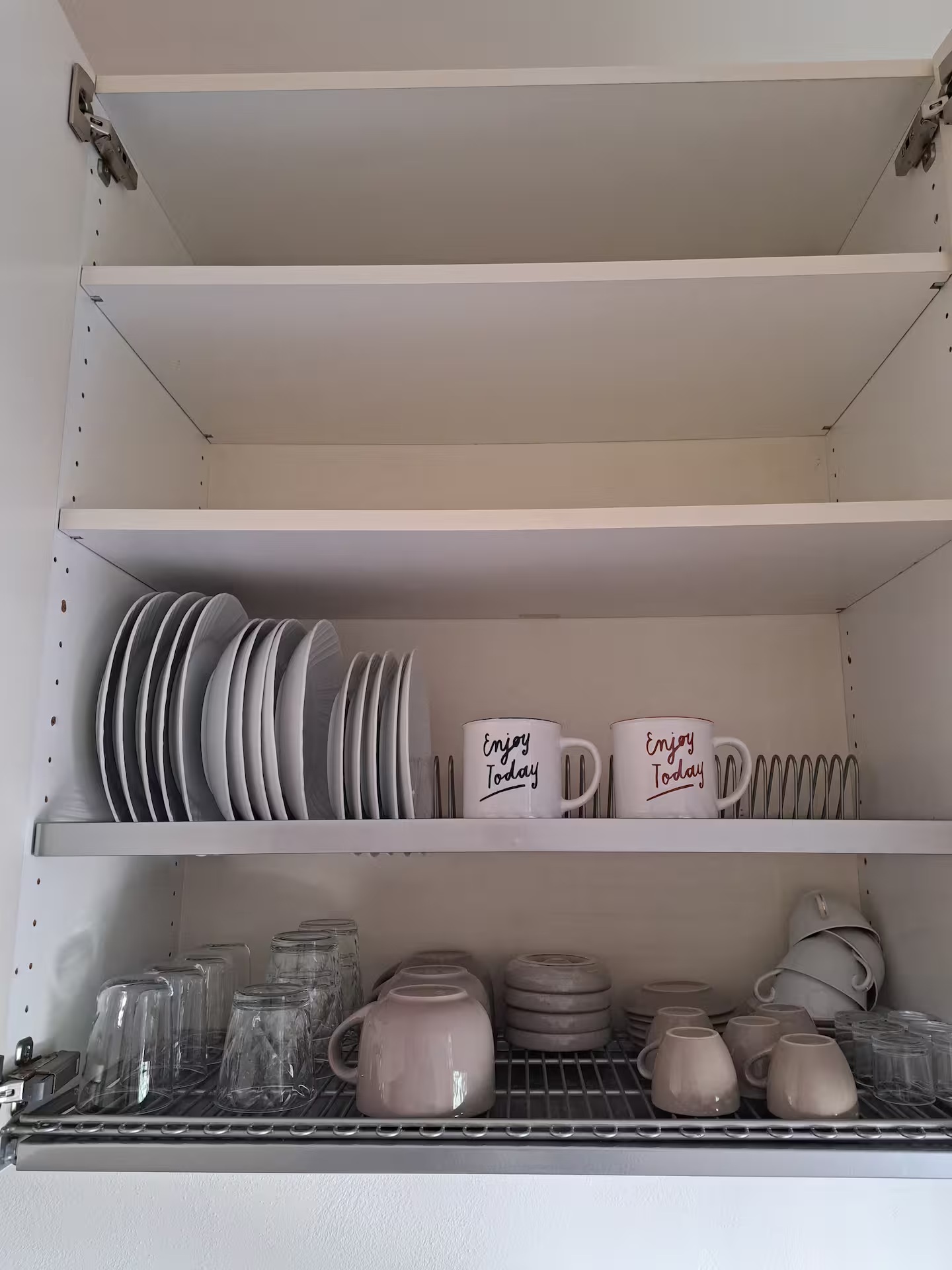 Open kitchen cabinet stocked with clean plates, glasses and espresso cups