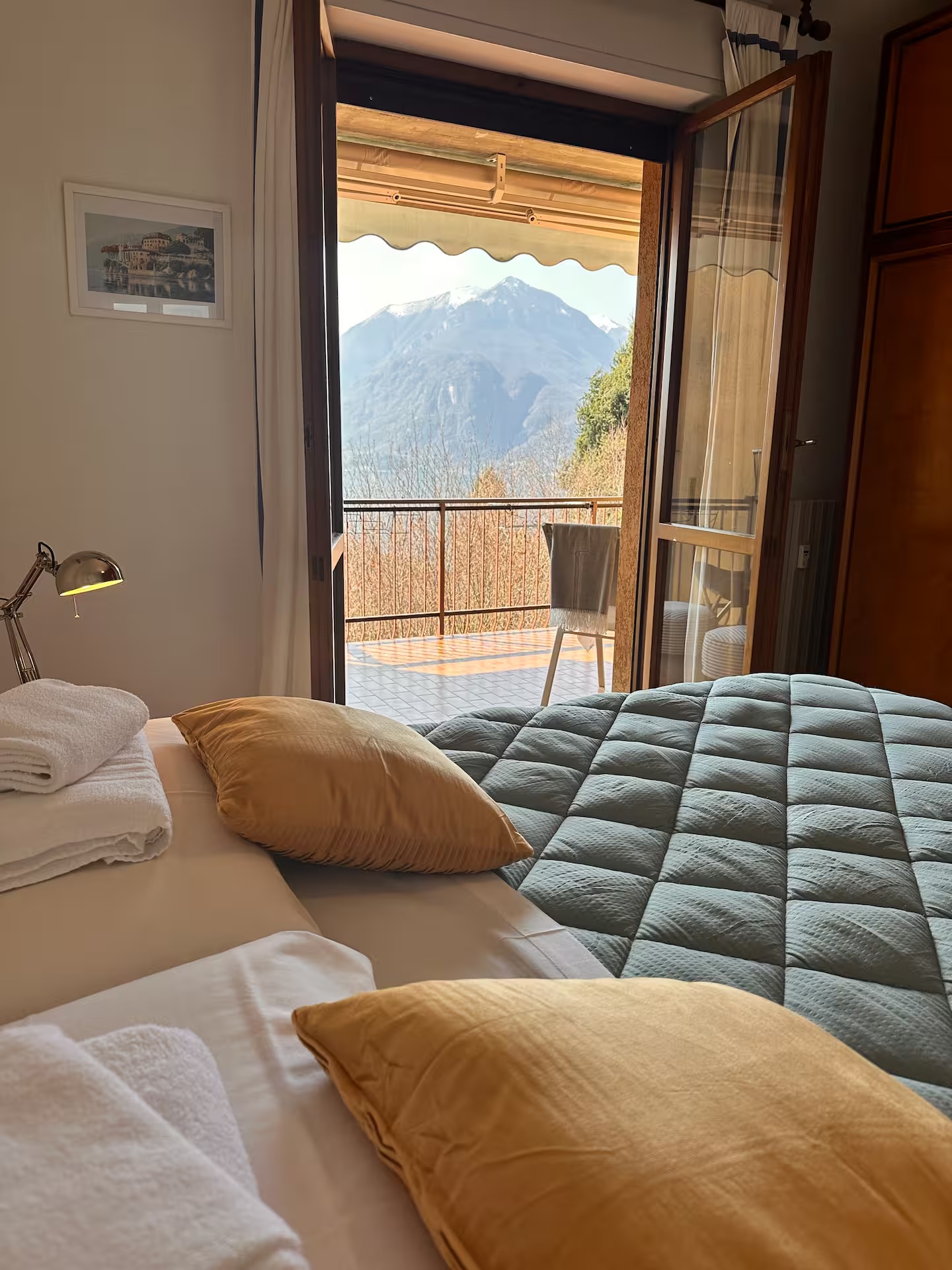 Bedroom with made bed, folded towels and open doors framing a mountain view